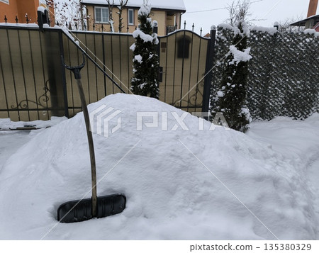 Snow shovel for clearing snow from a snowdrift and a fence behind it Snow shovel for clearing snow from a snowdrift and a fence behind it 135380329