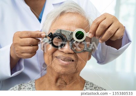 Asian senior woman wearing ophthalmic vision eye test and using optical trial frame. 135380533