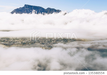 Aerial view of mountain peaks emerging from dense blanket clouds covering city Aerial view of mountain peaks emerging from dense blanket clouds covering city 135380554