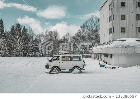 A caterpillar vehicle parked in a snowy field and a building in a snowy landscape 135380587