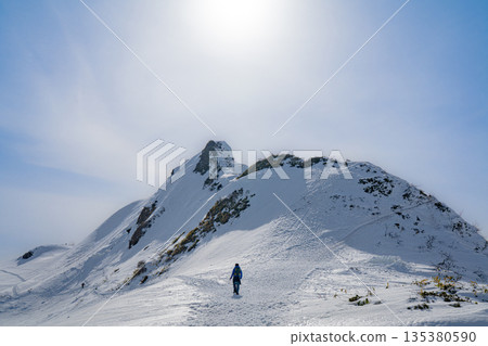 登山者走在背光的雪脊和冬季山脊線上。 登山者走在背光的雪脊和冬季山脊線上。 135380590