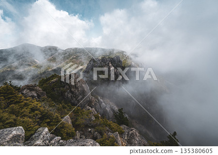 山景展現出嶙峋的山脊漂浮在雲霧繚繞之中，雲霧籠罩著山坡。 135380605