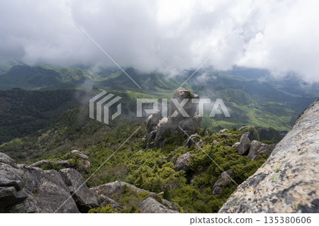Rocky peaks with clouds drifting through them and fresh green mountains 135380606