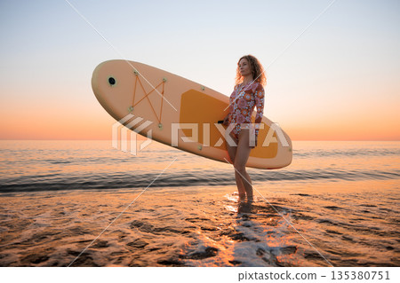 Young woman standing on beach with paddle sup boards during summer vacation Young woman standing on beach with paddle sup boards during summer vacation 135380751
