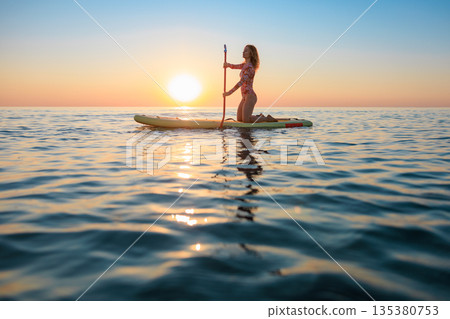 Young woman walking on stand up paddle sup boards by the sea during summer vacation 135380753