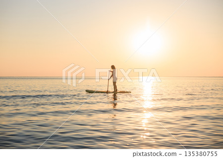 Young woman walking on stand up paddle sup boards by the sea during summer vacation 135380755