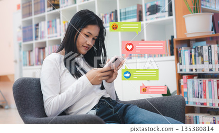 Young Asian Student Using Smartphone with Social Media Notification Icons in Library 135380814