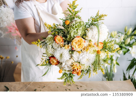 Person holds large bouquet featuring roses and hydrangeas over craft paper covered surface. Colorful wedding bouquet, maximalist floral design, trendy bridal flowers, vibrant wedding palette. Person holds large bouquet featuring roses and hydrangeas over craft paper covered surface. Colorful wedding bouquet, maximalist floral design, trendy bridal flowers, vibrant wedding palette. 135380909