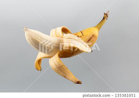 A peeled banana floating in the air against a gray background A peeled banana floating in the air against a gray background 135381051