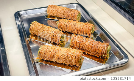 Traditional Turkish burma kadayif dessert with pistachios served on a metal tray in a local bakery Traditional Turkish burma kadayif dessert with pistachios served on a metal tray in a local bakery 135381714