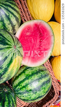 Fresh watermelons and yellow melons in a basket with one sliced watermelon showing ripe red pulp Fresh watermelons and yellow melons in a basket with one sliced watermelon showing ripe red pulp 135381829