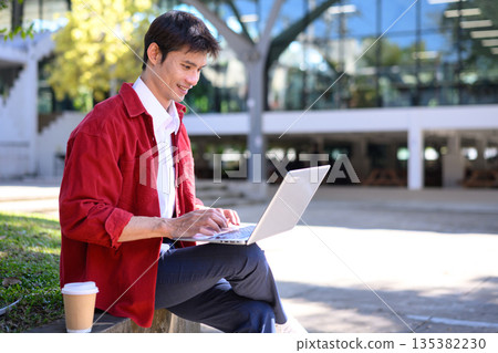 Professional man focused on work using a laptop outside a contemporary building, a serene outdoor setting 135382230