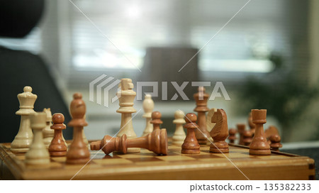 Checkmate. white chess queen piece knocking over king on a wooden chessboard Checkmate. white chess queen piece knocking over king on a wooden chessboard 135382233