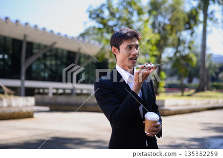 A man from an office walks outdoors talking on his phone while holding a coffee cup 135382259