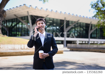A man from an office walks outdoors talking on his phone while holding a coffee cup 135382260