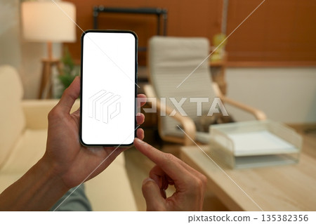 Close up view of a man using blank screen smartphone at living room Close up view of a man using blank screen smartphone at living room 135382356