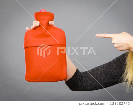 Woman holds hot water bottle in red fleece cover Woman holds hot water bottle in red fleece cover 135382745