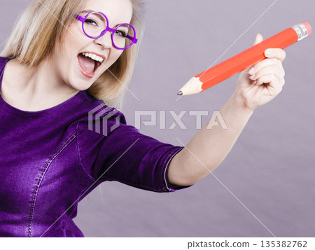 Happy woman holding big oversized pencil Happy woman holding big oversized pencil 135382762
