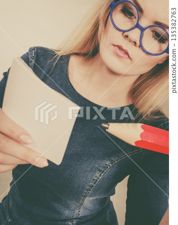 Serious woman holds big pencil note paper in hand Serious woman holds big pencil note paper in hand 135382763
