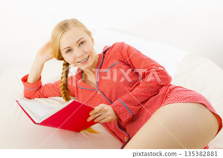 Woman relaxing in bed reading book Woman relaxing in bed reading book 135382881