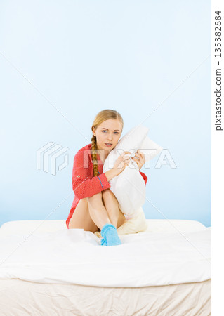 Young woman wearing pajamas hugging soft pillow 135382884