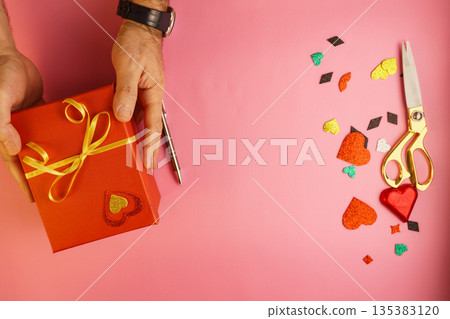 Man wrapping and decorating Valentine's gift box on pink background, DIY concept Man wrapping and decorating Valentine's gift box on pink background, DIY concept 135383120