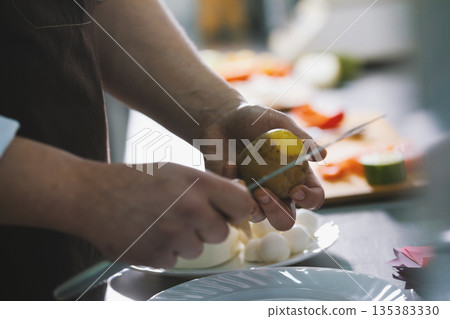 Chef is peeling potatoes for salad with knife in commercial kitchen Chef is peeling potatoes for salad with knife in commercial kitchen 135383330