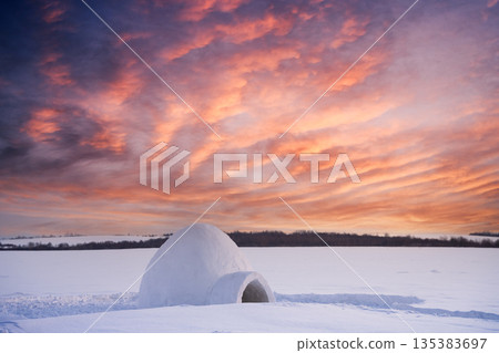 Snow igloo in the snowy field during incredible orange sunset Snow igloo in the snowy field during incredible orange sunset 135383697