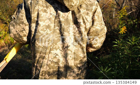 Rear view of ukrainian army soldier walking along trail at countryside. Young male military in uniform going through dry grass at sunny day. Invasion of territory Ukraine. Slow motion Rear view of ukrainian army soldier walking along trail at countryside. Young male military in uniform going through dry grass at sunny day. Invasion of territory Ukraine. Slow motion 135384149