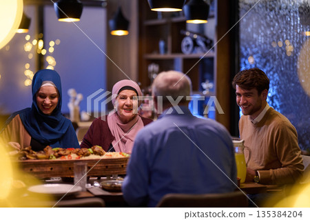 Muslim family enjoys iftar together at a restaurant decorated for Ramadan with traditional ornaments and warm lighting Muslim family enjoys iftar together at a restaurant decorated for Ramadan with traditional ornaments and warm lighting 135384204