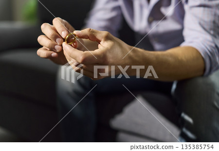 Stress and thinking about divorce of lonely man holding wedding ring in hands 135385754