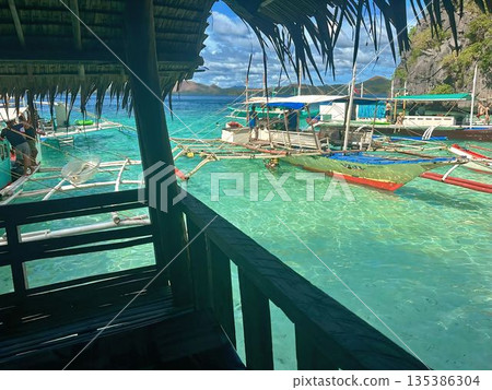 Tropical view of bangka boats in turquoise water from a wooden hut balcony 135386304
