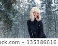 Portrait young adult mid age smile woman enjoy have fun walking in park forest snowfall cold winter day. Female portrait person happiness wear black ski overall stylish fur hat snowflakes background 135386616