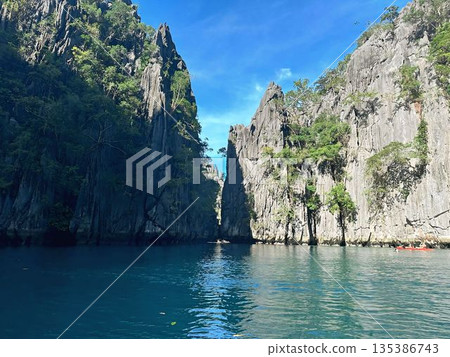 Majestic limestone karst cliffs rising from turquoise sea in a narrow tropical lagoon Majestic limestone karst cliffs rising from turquoise sea in a narrow tropical lagoon 135386743