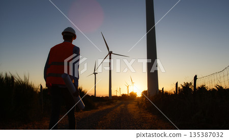 engineer walks at sunset under the wind turbines engineer walks at sunset under the wind turbines 135387032