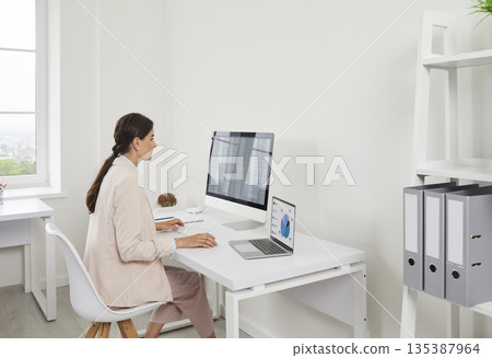 Businesswoman reviewing charts on laptop and desktop computer in modern office 135387964