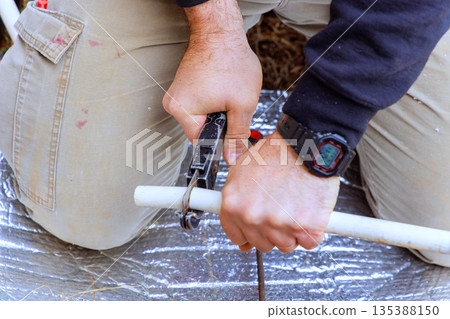 Person using tool to work on white pipe in backyard 135388150