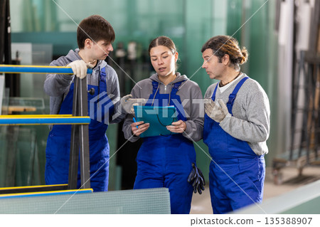 Girl and two male glazier employees with documents speaking and advising in workshop 135388907