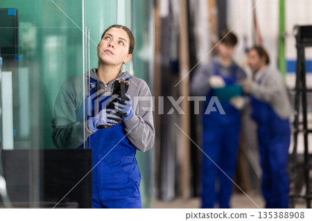 Young woman measuring sheet of glass with device 135388908