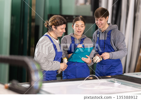 Girl and two male glazier employees with documents speaking and advising in workshop Girl and two male glazier employees with documents speaking and advising in workshop 135388912