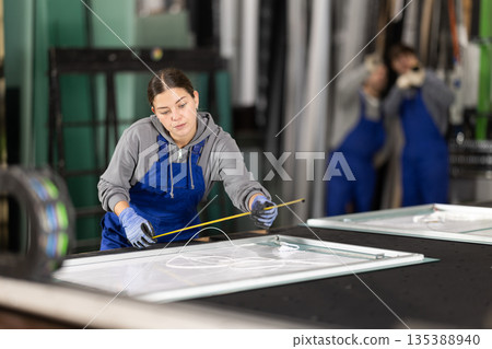 Young woman employee in blue overall measures given length of plastic material Young woman employee in blue overall measures given length of plastic material 135388940