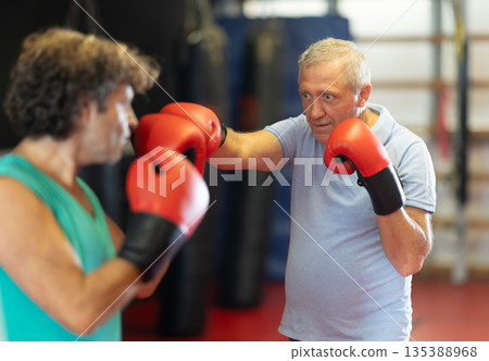 Older man in boxing gloves landing punch in self-defense sparring 135388968