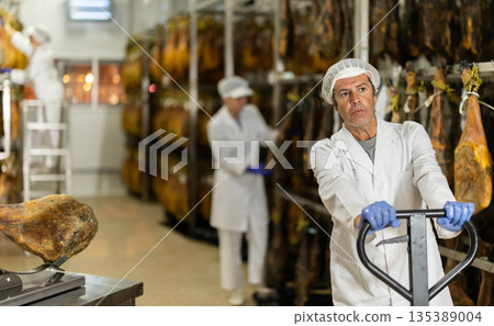 man factory worker prepares to load jamon onto a pallet truck 135389004