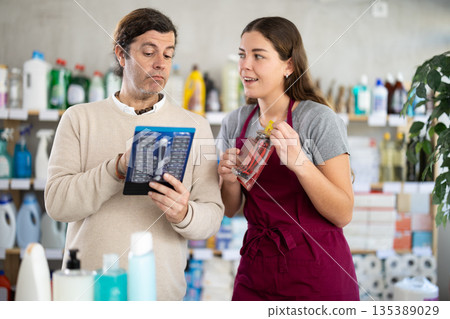 Smiling female shop assistant offering razor to male customer Smiling female shop assistant offering razor to male customer 135389029