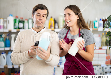 Saleswoman offering shower gel to man scanning barcode of bottles in store Saleswoman offering shower gel to man scanning barcode of bottles in store 135389031