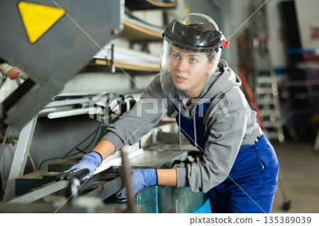 Girl employee wearing safety face shield performs hazardous work in production. 135389039