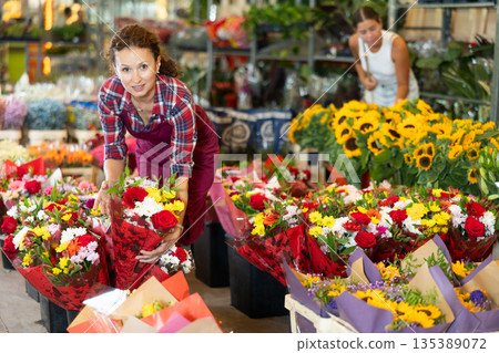 Positive female seller in apron holds designer bouquet in hands 135389072