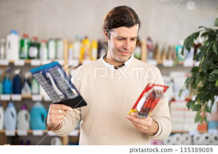 Among shop windows, man buyer leisurely examines goods and chooses razor 135389089
