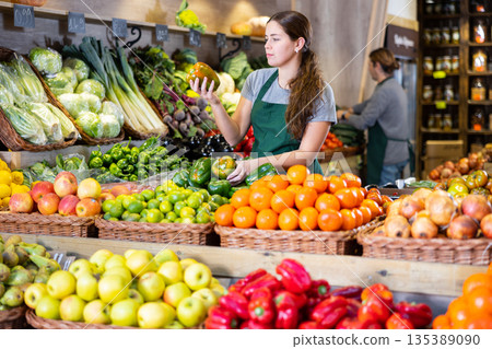 Female seller holding green peppers standing in fruit and vegetable section of supermarket 135389090