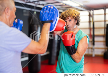 Man punches boxing paw held by trainer Man punches boxing paw held by trainer 135389199